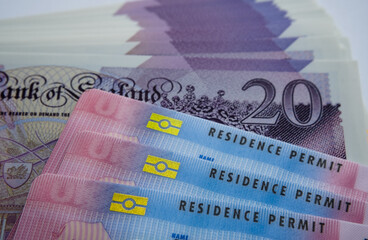 UK Biometric Residence permit cards and 20 pound banknotes. BRP cards released for Tier 2 work visa immigrants. Concept image for price of the visa.