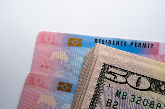 UK Biometric Residence permit cards and stack of 50 dollar banknotes. BRP cards released for Tier 2 work visa immigrants. Concept image for cost of the visa.