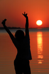 Fototapeta premium silhouette of woman admiring the sunset in golden, yellow and red tones, with the sun descending over the waters of a river