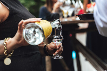 Woman pouring alcohol into glass. Closeup of female hands pouring transparent alcoholic drink from bottle. Celebration, birthday, party, wedding