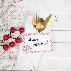 Christmas Table Place Setting with Gold Silverware, red berries, and white napkin, all on a White Shiplap Wood Board Background.  The Name Card provides copy space.