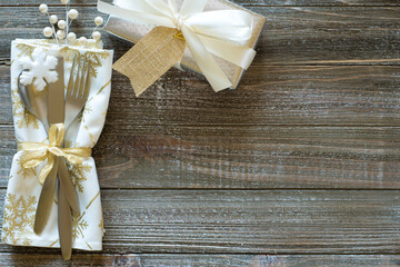 Wintry Christmas Table Place Setting with Snowflake napkin, Silver present with white bow and berries, all on rustic wood boards background.