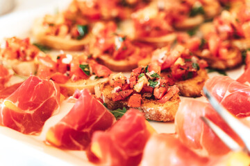 Tasty mini sandwich snacks and fruit rolled in ham on white tray on buffet table. Shallow depth of field. Celebration, party, birthday or wedding