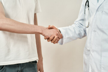 Doctor and patient shaking hands while standing against grey background. Close up