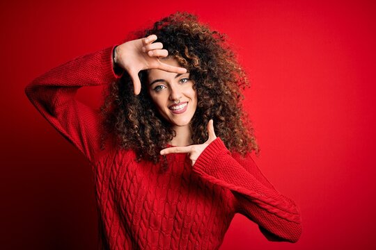 Young beautiful woman with curly hair and piercing wearing casual red sweater smiling making frame with hands and fingers with happy face. Creativity and photography concept.
