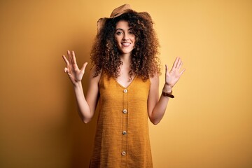 Beautiful brunette woman on vacation with curly hair and piercing wearing hat and dress showing and...