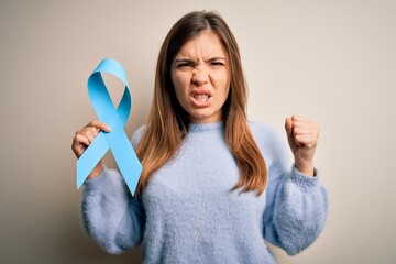 Young blonde woman holding prostate cancer awareness campaing blue ribbon annoyed and frustrated...