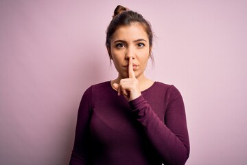 Beautiful young woman wearing casual bun hairstyle over pink isolated background asking to be quiet with finger on lips. Silence and secret concept.