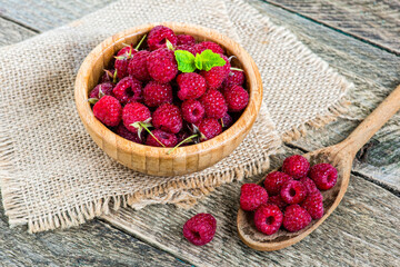 Ripe sweet and fresh raspberries in bowl with mint leaves and wooden spoon on vintage wood table.
