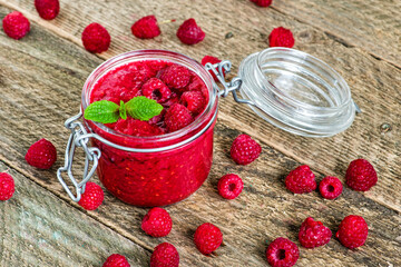 Summer pink raspberry smoothie in a jar with berries and mint leaves on a rustic wood background.