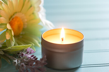Lighted and Scented Candle in a tin holder with flowers on the side, all on teal boards table...