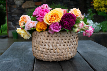 Colorful bouquet of roses, pink, red, burgundy in a wicker basket. Garden party