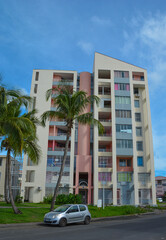 Point-a-Pitre, Guadeloupe - Sept 17, 2018: Colorful residential building of local people on the street with green palm trees, road and a parked car