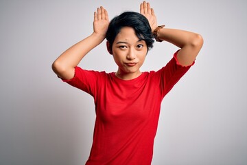 Young beautiful asian girl wearing casual red t-shirt standing over isolated white background Doing bunny ears gesture with hands palms looking cynical and skeptical. Easter rabbit concept.