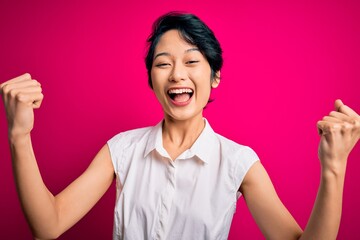 Young beautiful asian girl wearing casual summer shirt standing over isolated pink background celebrating surprised and amazed for success with arms raised and open eyes. Winner concept.