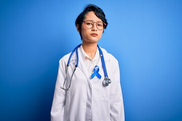Fototapeta premium Young beautiful asian doctor girl wearing stethoscope and coat with blue cancer ribbon skeptic and nervous, frowning upset because of problem. Negative person.
