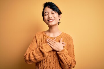 Young beautiful asian girl wearing casual sweater and diadem standing over yellow background...