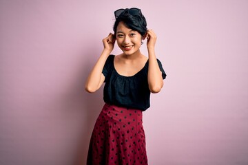 Young beautiful asian girl wearing casual dress standing over isolated pink background Smiling pulling ears with fingers, funny gesture. Audition problem