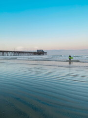 Surfer heading into ocean at sunset at Newport Beach Pier 
