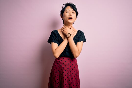 Young beautiful asian girl wearing casual dress standing over isolated pink background shouting suffocate because painful strangle. Health problem. Asphyxiate and suicide concept.