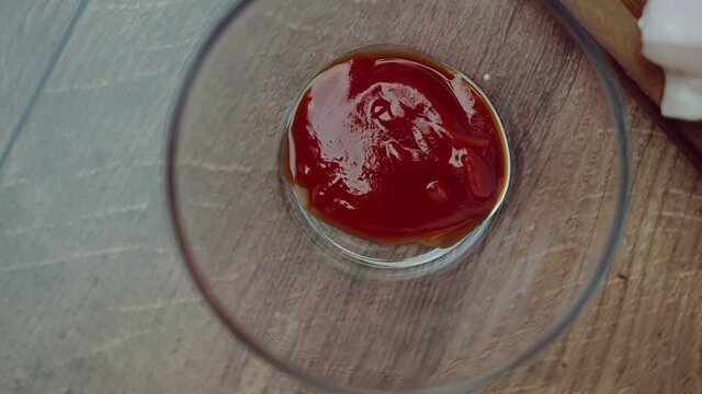 A measure of 1 TBSP of Tomato Ketchup in a transparent glass bowl on a brown wooden table. Rotating camera capturing a food ingredient.