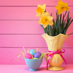 Colorful Easter Eggs in Nest with Daffodils in Vase on Pink Boards Background with room or space for copy, text, or your words.  Vertical