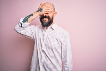 Handsome bald man with beard wearing elegant shirt over isolated pink background smiling and laughing with hand on face covering eyes for surprise. Blind concept.