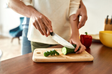 Cropped shot of woman cutting vegetables while man helping, touching her hands, standing behind her. Vegetarians preparing healthy meal in the kitchen together