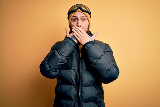 Handsome skier bald man with beard skiing wearing snow sportswear and ski goggles shocked covering mouth with hands for mistake. Secret concept.