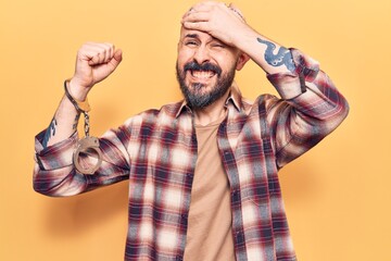 Young handsome man wearing prisoner handcuffs stressed and frustrated with hand on head, surprised and angry face