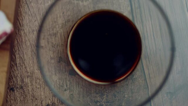 A measure of 1 TBSP of Soya sauce in a transparent glass bowl on a brown wooden table. Rotating camera capturing a food ingredient.