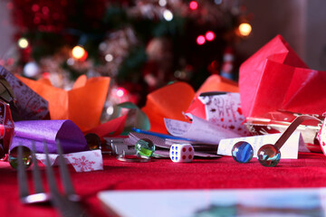Shallow depth of field image of a Christmas table. Christmas crackers have been opened and the toys and prizes laid out. Focus is on the dice and a marble. in the background the Christmas tree lights.