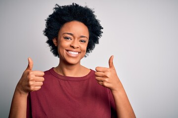 Young beautiful African American afro woman with curly hair wearing casual t-shirt standing success sign doing positive gesture with hand, thumbs up smiling and happy. Cheerful expression and winner