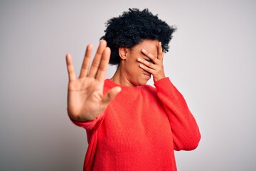 Fototapeta na wymiar Young beautiful African American afro woman with curly hair wearing red casual sweater covering eyes with hands and doing stop gesture with sad and fear expression. Embarrassed and negative concept.