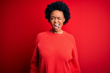 Fototapeta na wymiar Young beautiful African American afro woman with curly hair wearing casual sweater sticking tongue out happy with funny expression. Emotion concept.