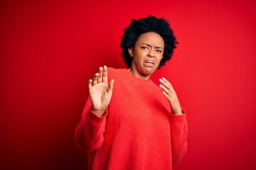 Young beautiful African American afro woman with curly hair wearing casual sweater disgusted...