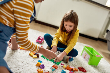 Game. Caucasian cute little girl spending time with african american baby sitter. They are playing with toys, sitting on the floor