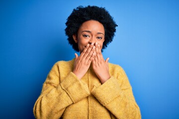 Young beautiful African American afro woman with curly hair wearing yellow casual sweater laughing and embarrassed giggle covering mouth with hands, gossip and scandal concept