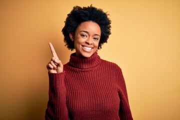 Young beautiful African American afro woman with curly hair wearing casual turtleneck sweater pointing finger up with successful idea. Exited and happy. Number one.