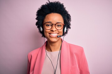 Young African American call center operator woman with curly hair using headset with a happy and...