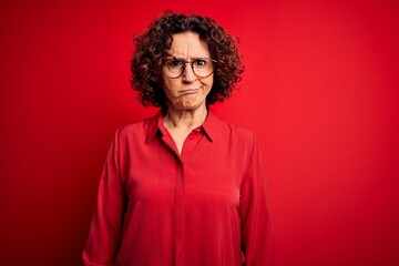 Obraz na płótnie Canvas Middle age beautiful curly hair woman wearing casual shirt and glasses over red background skeptic and nervous, frowning upset because of problem. Negative person.