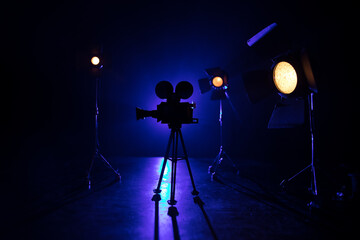 Movie concept. Miniature movie set on dark toned background with fog and empty space. Silhouette of vintage camera on tripod.