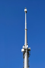 A mast with telecommunication equipment on a background of blue summer sky.
