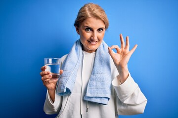 Middle age beautiful blonde sportswoman wearing towel drinking glass of water to refreshment doing ok sign with fingers, excellent symbol