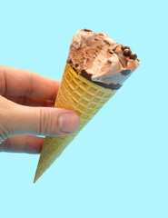 hand holding a fresh chocolate flavor ice cream cone with a bite on a blue background