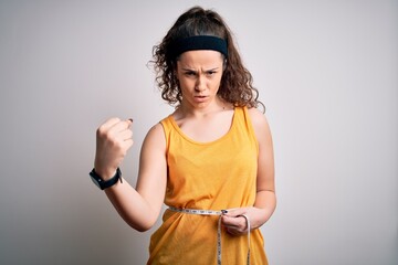 Young beautiful woman with curly hair controlling weight using tape mesure annoyed and frustrated shouting with anger, crazy and yelling with raised hand, anger concept