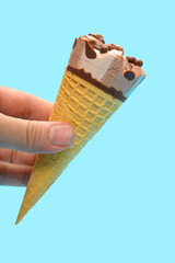hand holding a fresh chocolate flavor ice cream cone on a blue background