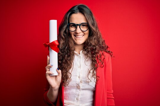 Young beautiful woman with curly hair holding university diploma degree over red background with a happy face standing and smiling with a confident smile showing teeth