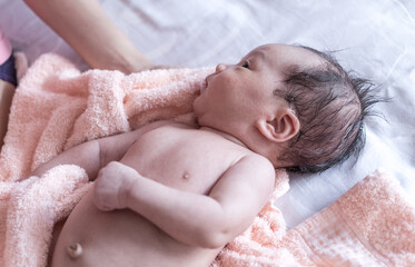newborn baby lying in a bath towel on the bed with mother hands holding towel