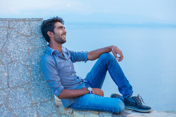 Man posing while standing near a concrete wall bridge above the sea